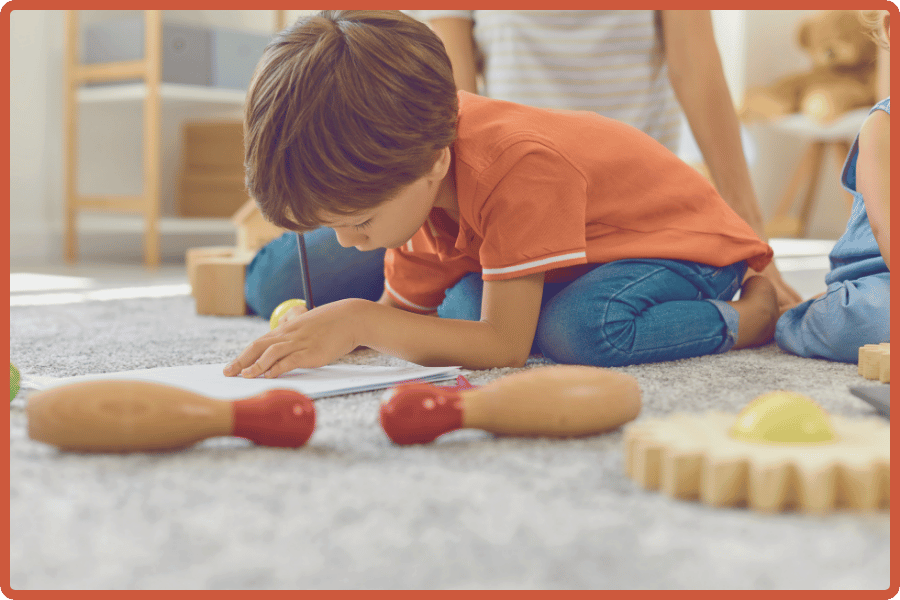 Young boy sitting casually on a classroom carpet, intently working on a project.