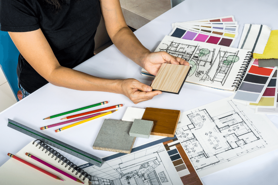 Architect student at desk, surrounded by architecture flat file plans and design samples, deep in work.