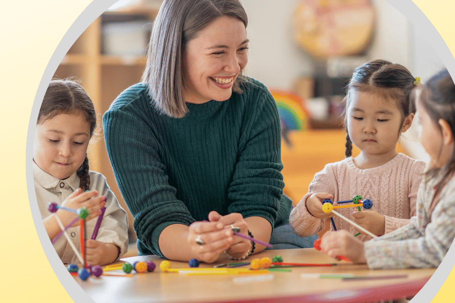 Kindergarten students sitting at an activity table with their teacher while working on a project. 