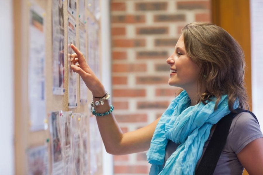 Female student pointing at notices on a school bulletin board.