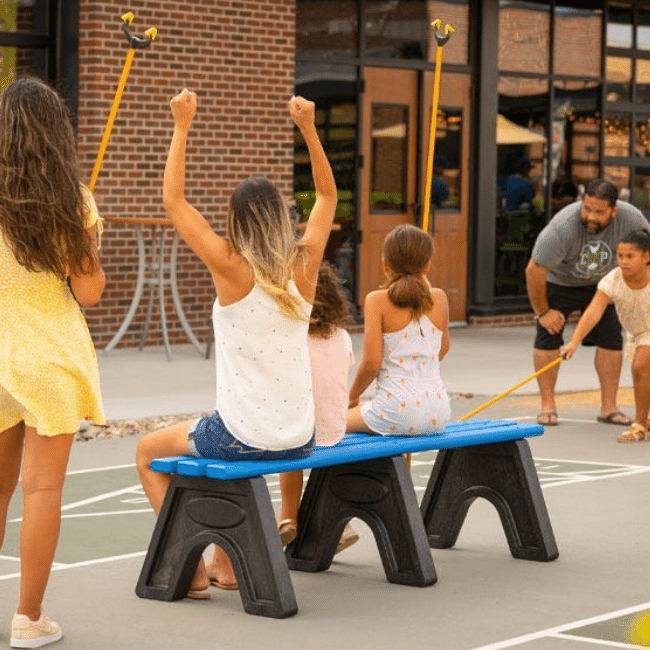 Students sit on a bench outdoors cheering their classmates as they play a game on the playground. 