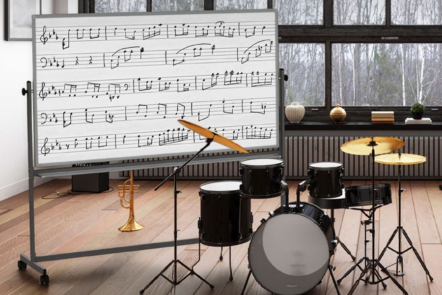 Mobile whiteboard with printed music staff lines and handwritten notes beside drums and a trumpet in a music room.